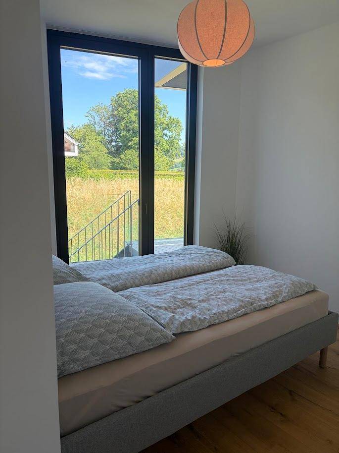 Helles Schlafzimmer mit zwei Einzelbetten, Holzboden und großen Fenstern mit Blick auf die Natur.