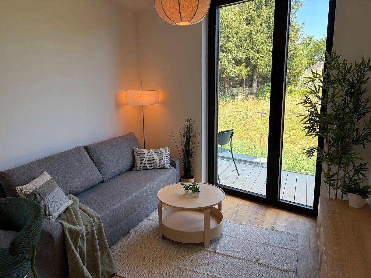Gemütlicher Wohnbereich mit grauem Sofa, Couchtisch und bodentiefen Fenstern mit Zugang nach draußen.