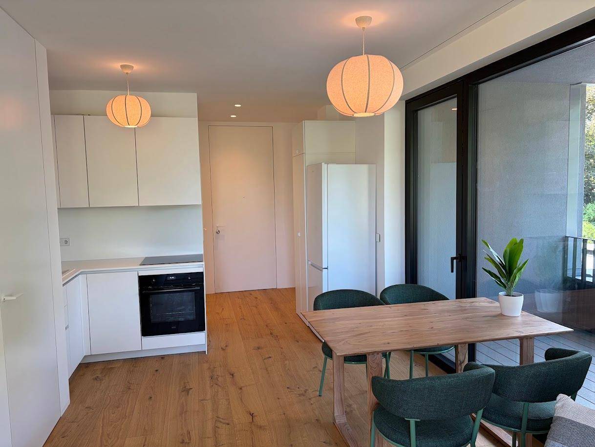 Moderne Einbauküche mit weißen Schränken, integrierten Geräten und offenem Essbereich mit Holztisch.