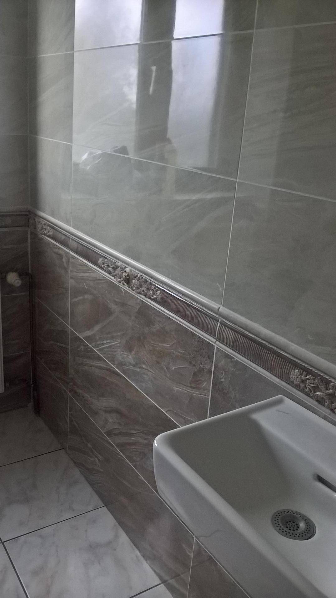 Kleines WC mit modernem Waschbecken und grauen Fliesen an den Wänden.