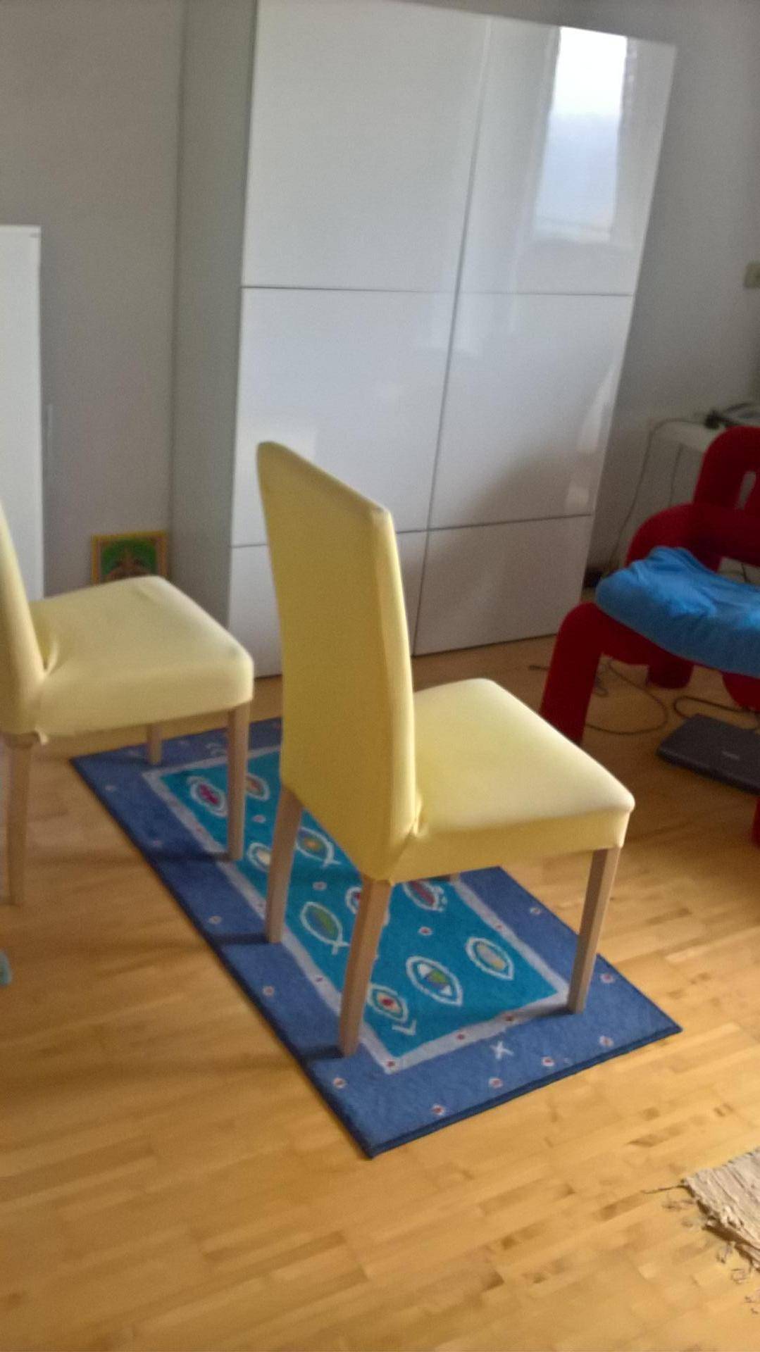 Heller Raum mit gelben Stühlen, Teppich und weißem Kleiderschrank.