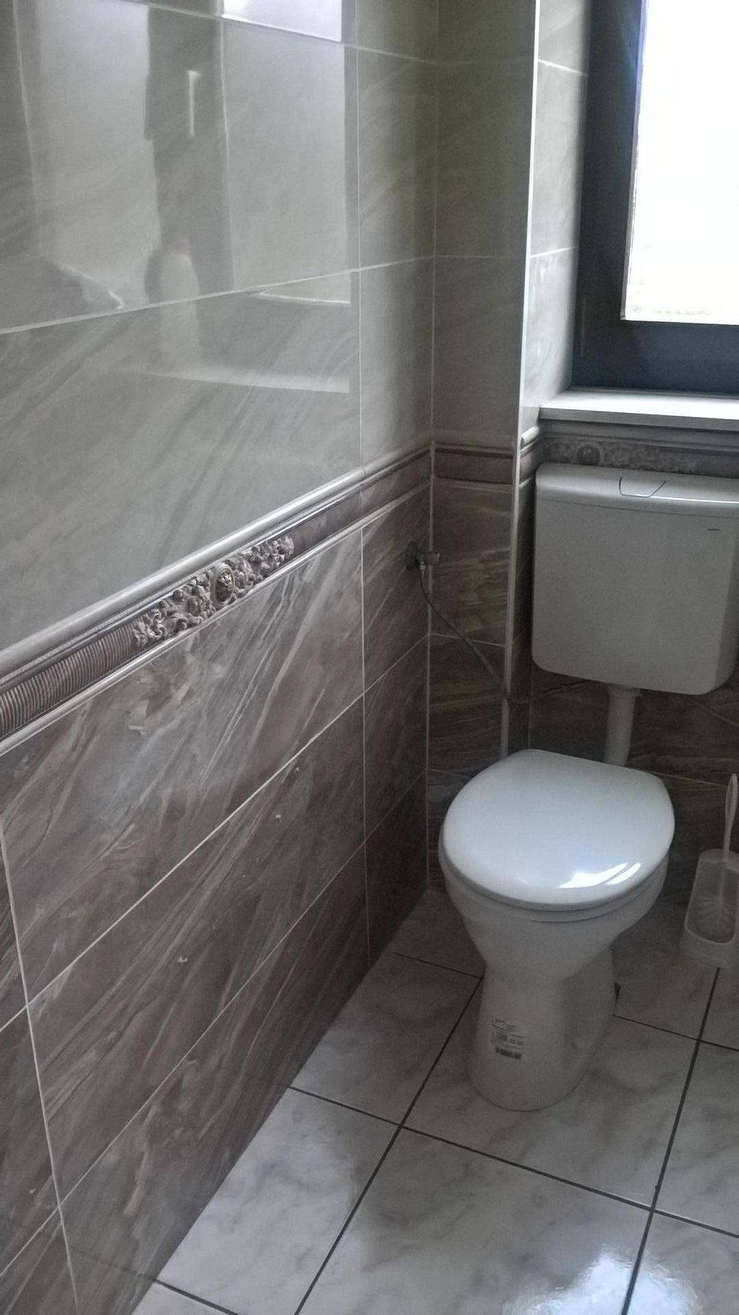 Modern gefliestes WC mit Fenster und einfacher Toilette.