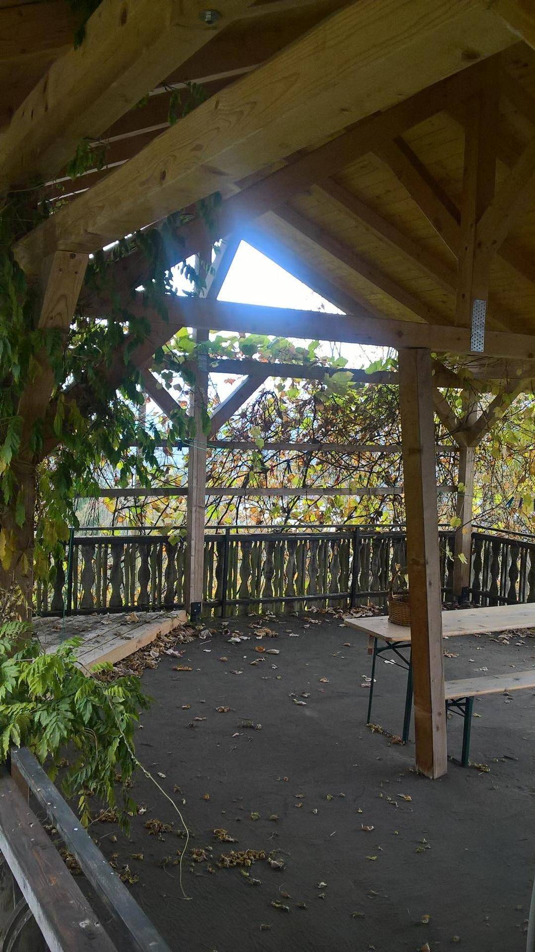 Rustikale Holzpergola mit Sitzgelegenheiten und Blick ins Grüne.