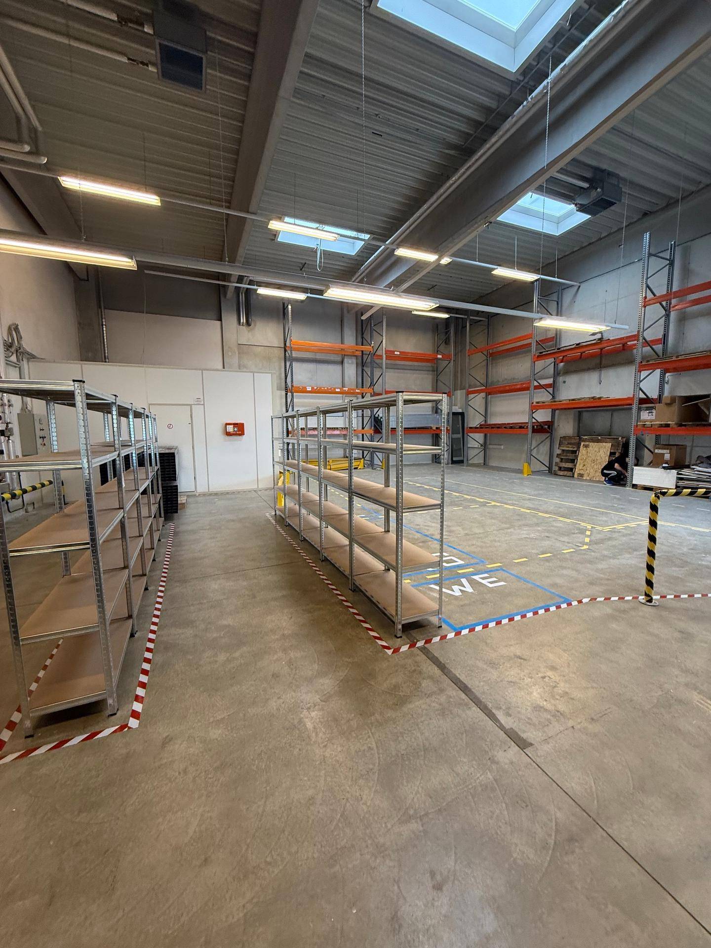 Weitläufige Lagerfläche mit Regalsystemen, Betonboden und Oberlichtern für ausreichend Tageslicht.