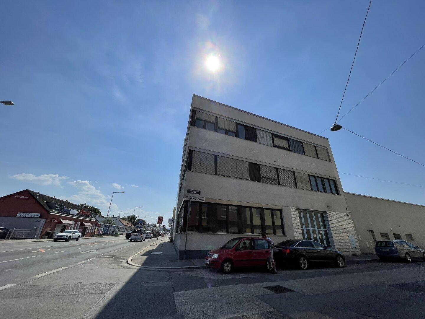 Ansicht des modernen Bürogebäudes von der Straße aus mit viel Sonnenlicht und umliegenden Fahrzeugen.