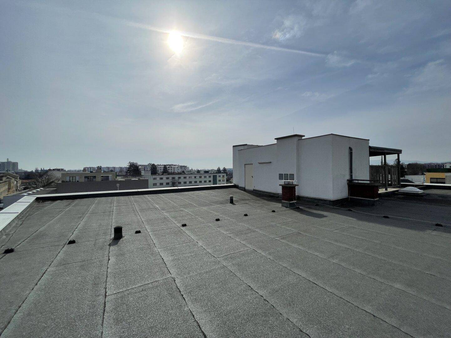 Flachdach des Gebäudes mit weitem Blick über die Stadt und umliegende Bebauung unter strahlendem Himmel.