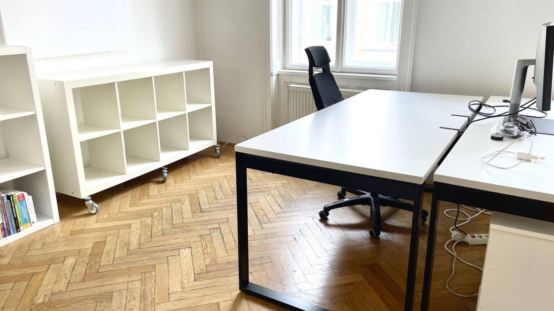 Helles Büro mit modernem Schreibtisch, Bürostuhl und Regalen auf Fischgrätparkett.