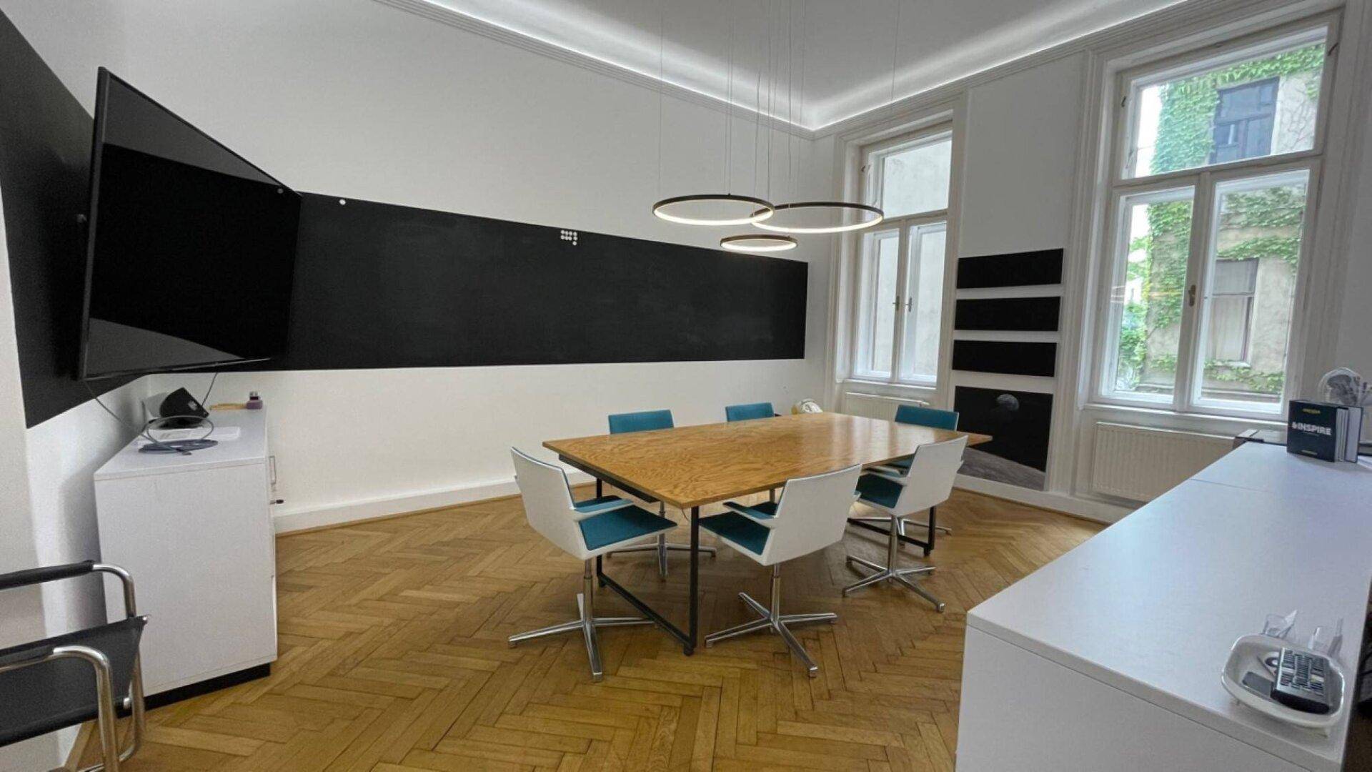 Moderner Konferenzraum mit großem Holztisch, bequemen Stühlen und Wandfernseher auf Fischgrätparkett.