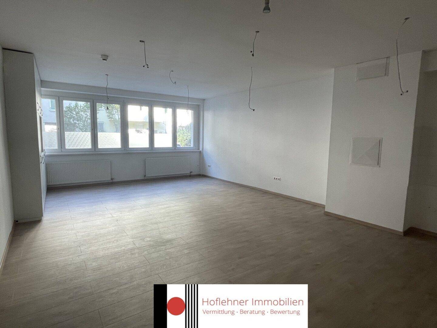 Leerer Raum mit Holzoptikboden und großen Fenstern, ideal für Büronutzung oder als Arbeitsbereich.