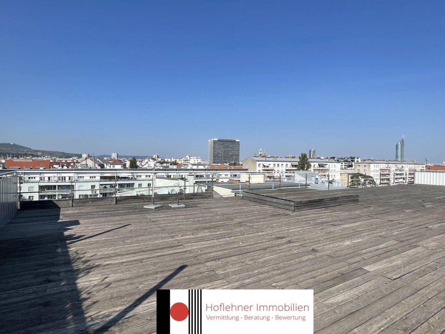 Weitläufige Dachterrasse mit Holzboden und Panoramablick über die Stadt, ideal zum Entspannen.