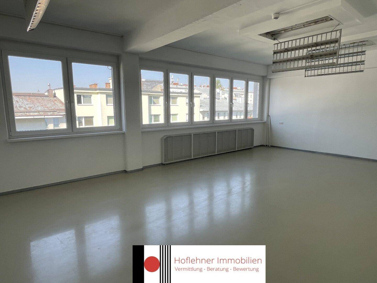 Heller Büroraum mit vielen Fenstern und Blick auf die umliegenden Gebäude, gut beleuchtet.