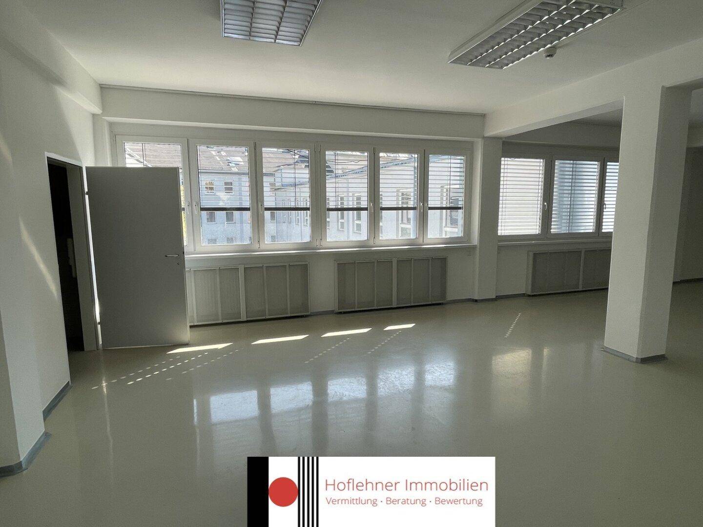 Heller Büroraum mit Fensterfront und Jalousien, der viel natürliches Licht bietet.
