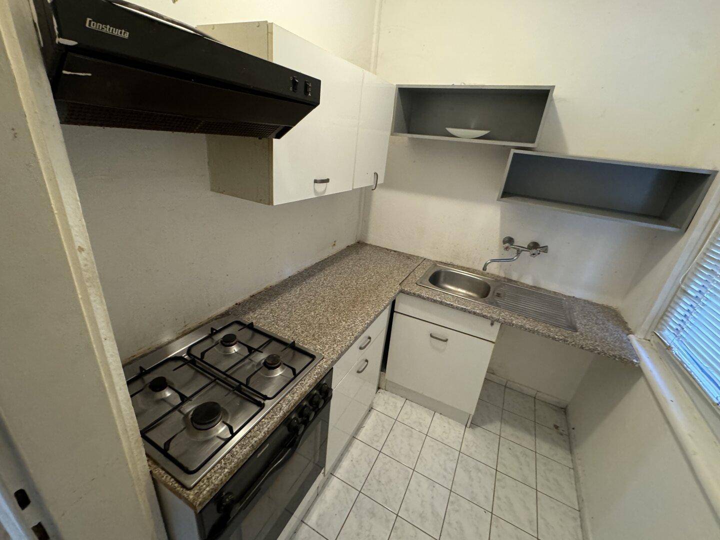 Kleine Küche mit Gasherd, Backofen, Spüle und einfachen weißen Schränken, funktional ausgestattet.