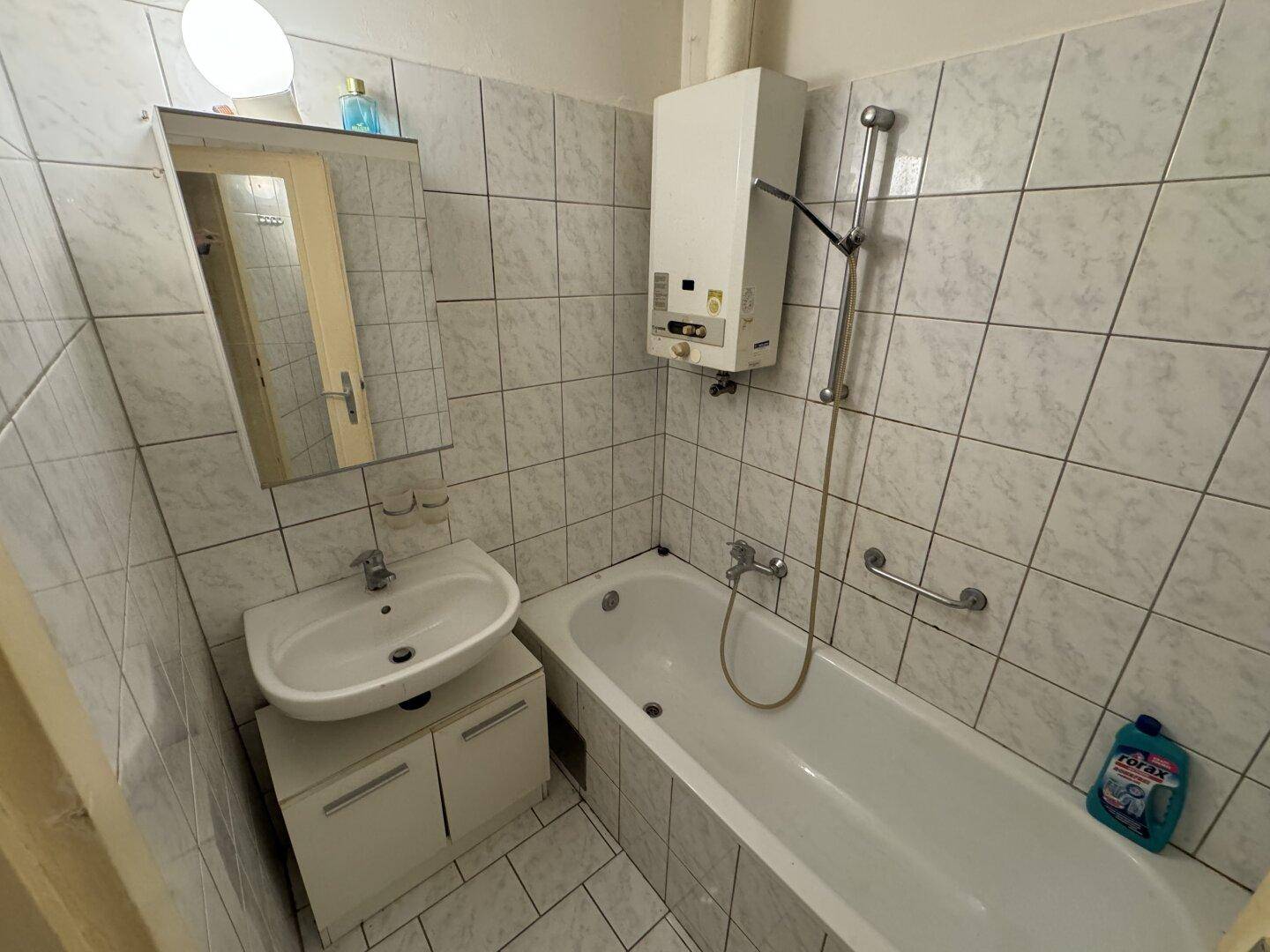 Badezimmer mit Badewanne, Waschbecken, Spiegel und Wandfliesen, inklusive Warmwasserbereiter.