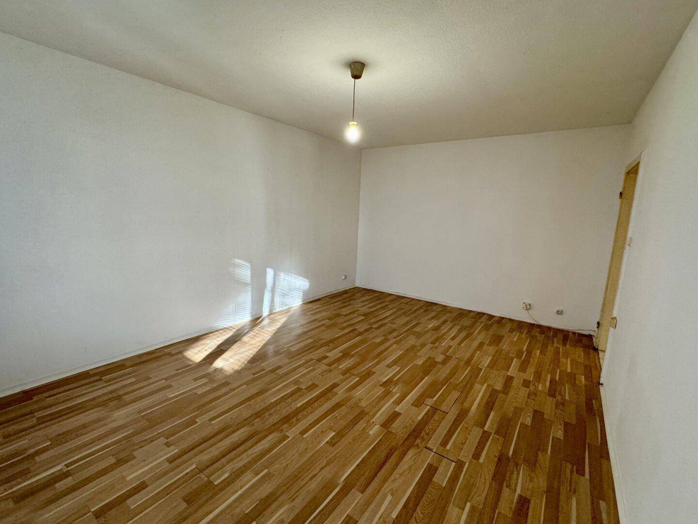 Geräumiges, leeres Zimmer mit hellem Parkettboden und neutralen Wänden, bereit zur individuellen Gestaltung.