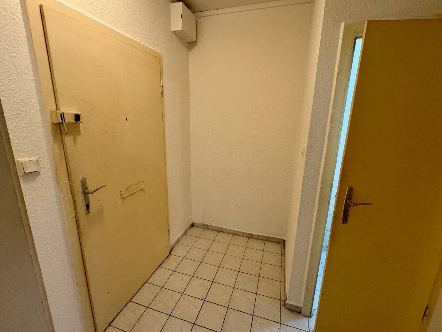 Eingangsbereich mit Fliesenboden, zwei Türen und Gegensprechanlage, die zu den Wohnräumen führt.