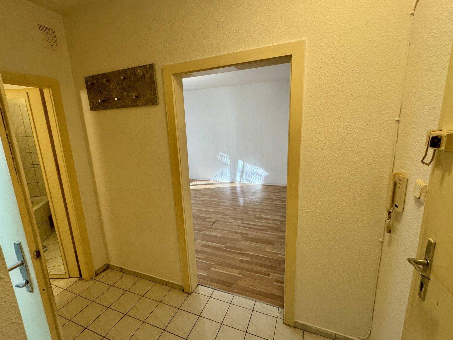 Flur mit Fliesenboden und Garderobe, der den Blick in ein angrenzendes Zimmer freigibt.
