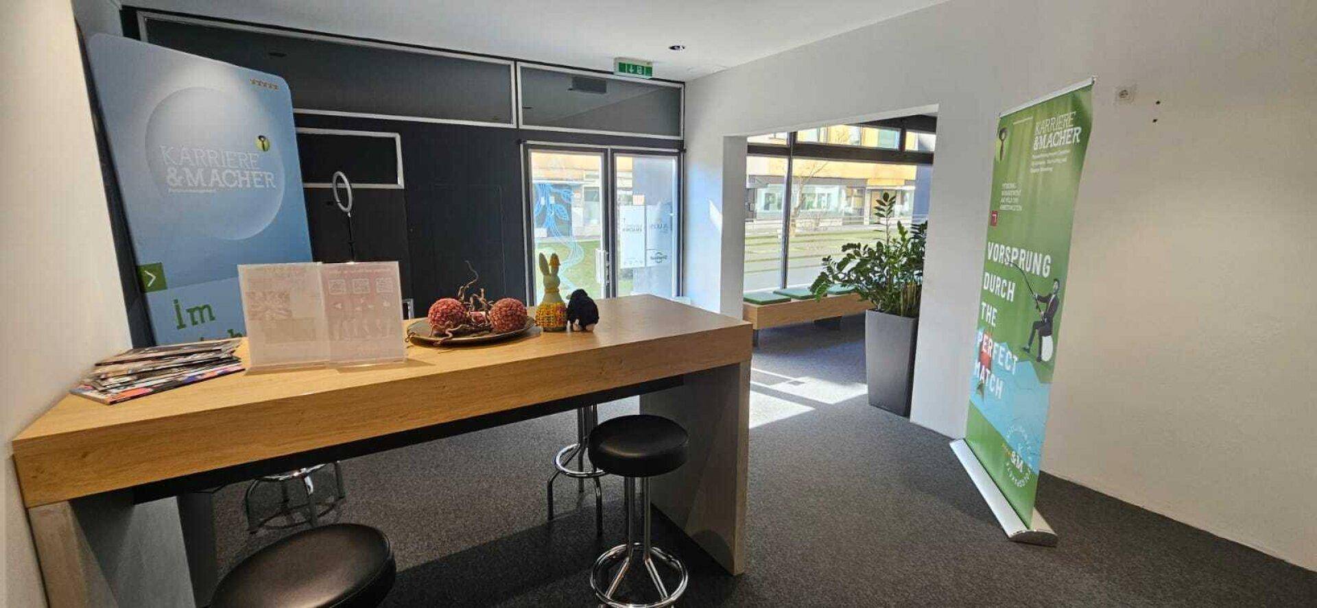 Informeller Bürobereich mit Stehtisch, Barhockern und Blick auf den Wartebereich.