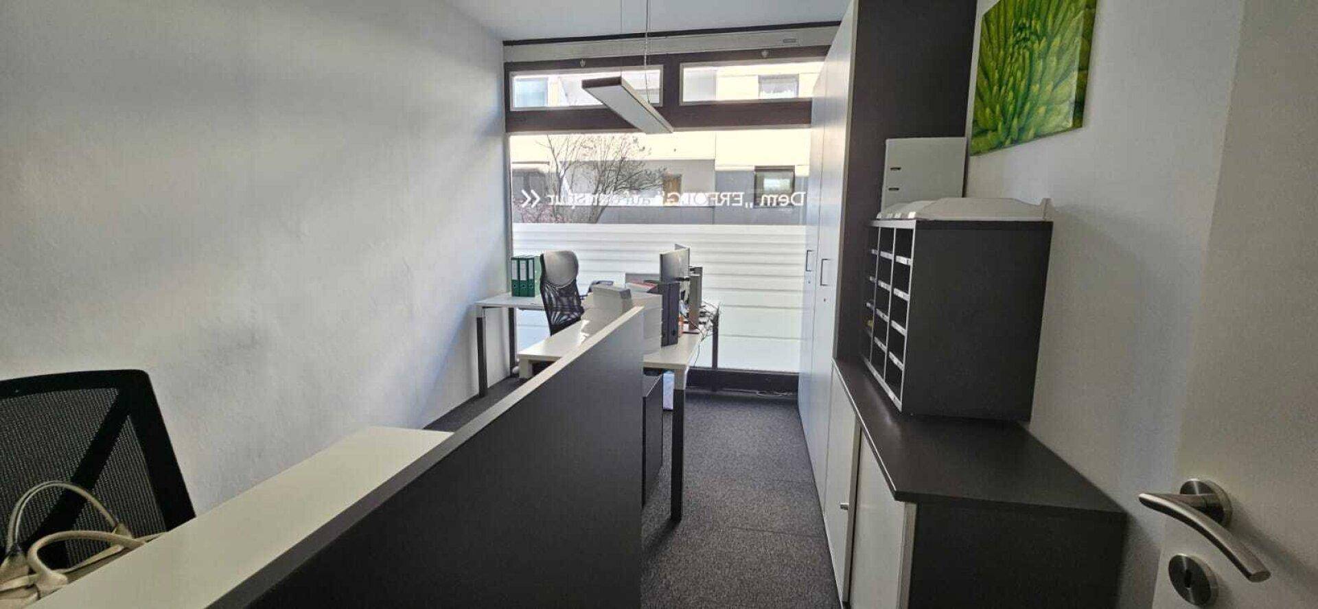 Kleines Büro mit Schreibtisch, Bürostuhl und Fenster mit Blick nach draußen.
