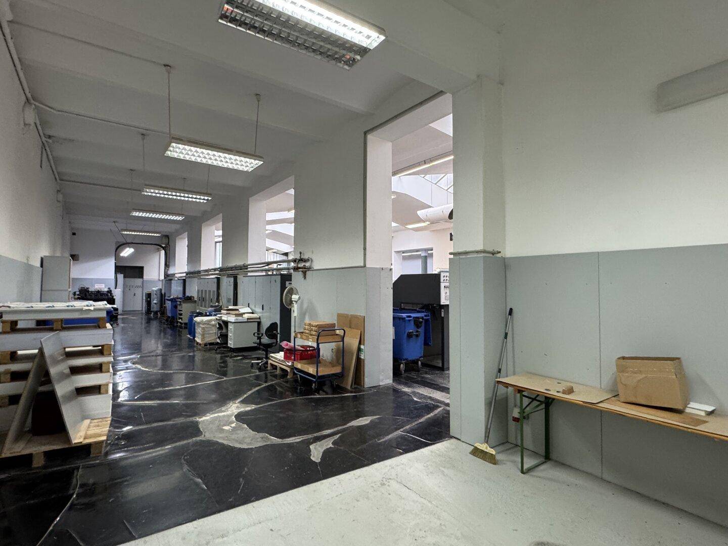 Industrieller Gang mit glänzendem dunklem Boden, Maschinen und hohen Decken, die ein geräumiges Gefühl vermitteln.