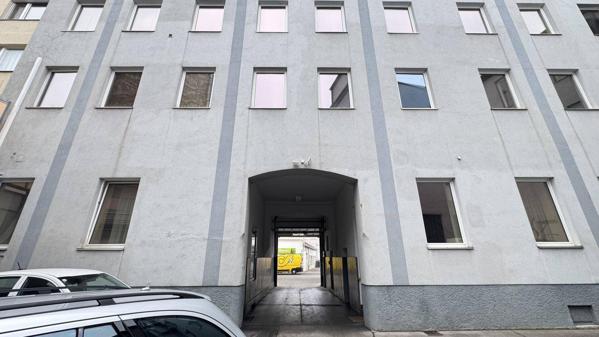 Fassade eines Mehrfamilienhauses mit vielen Fenstern und einem großen Torbogen als Eingangsbereich.