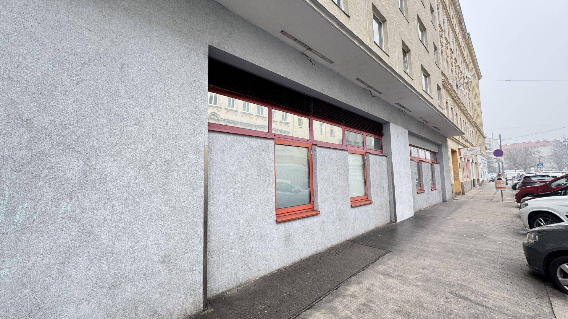 Gebäudefassade an einer Straße mit roten Fensterrahmen und Parkplätzen entlang des Bürgersteigs.