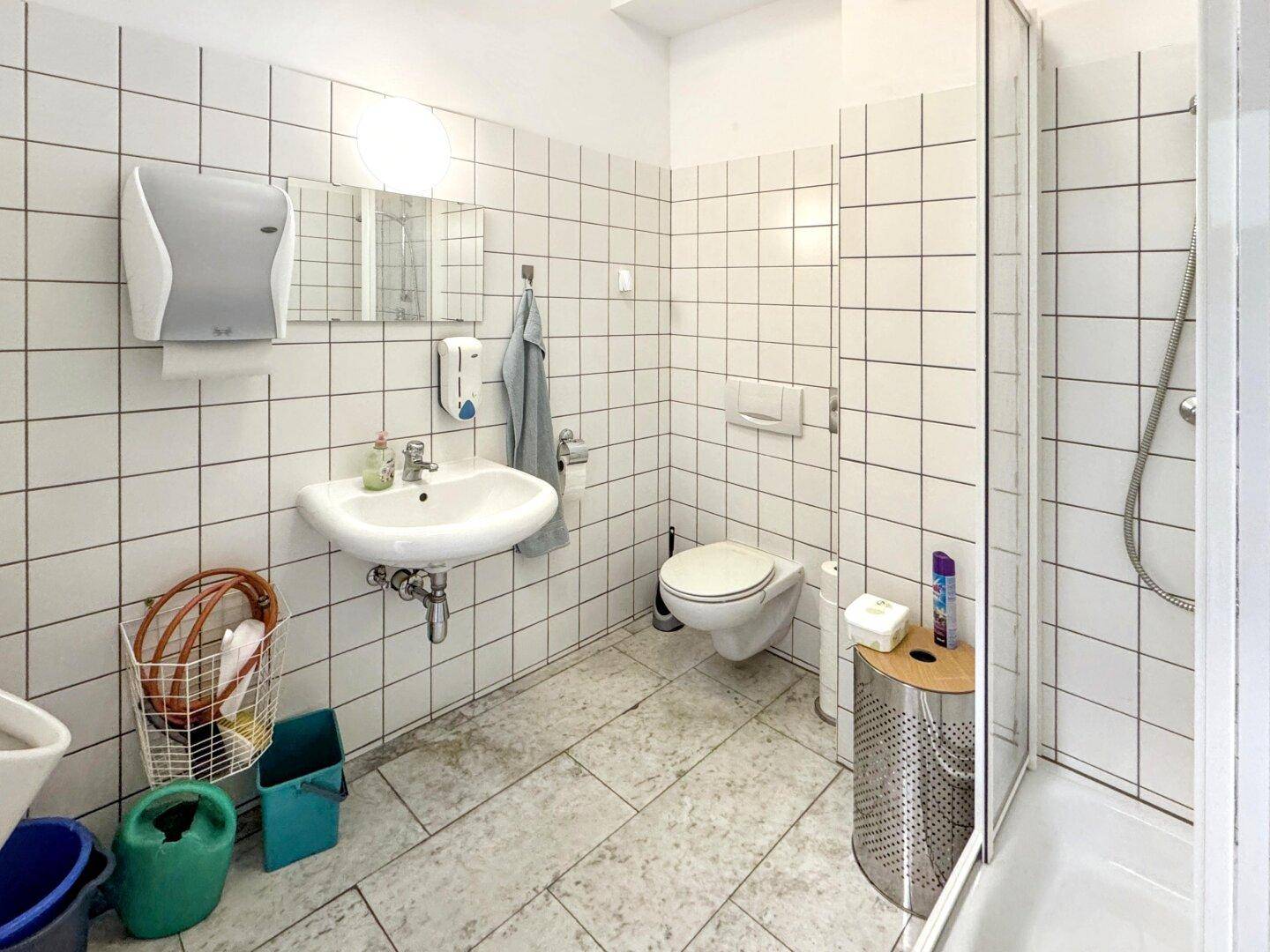 Badezimmer mit weißen Fliesen, Waschbecken, Toilette und einer Duschkabine.