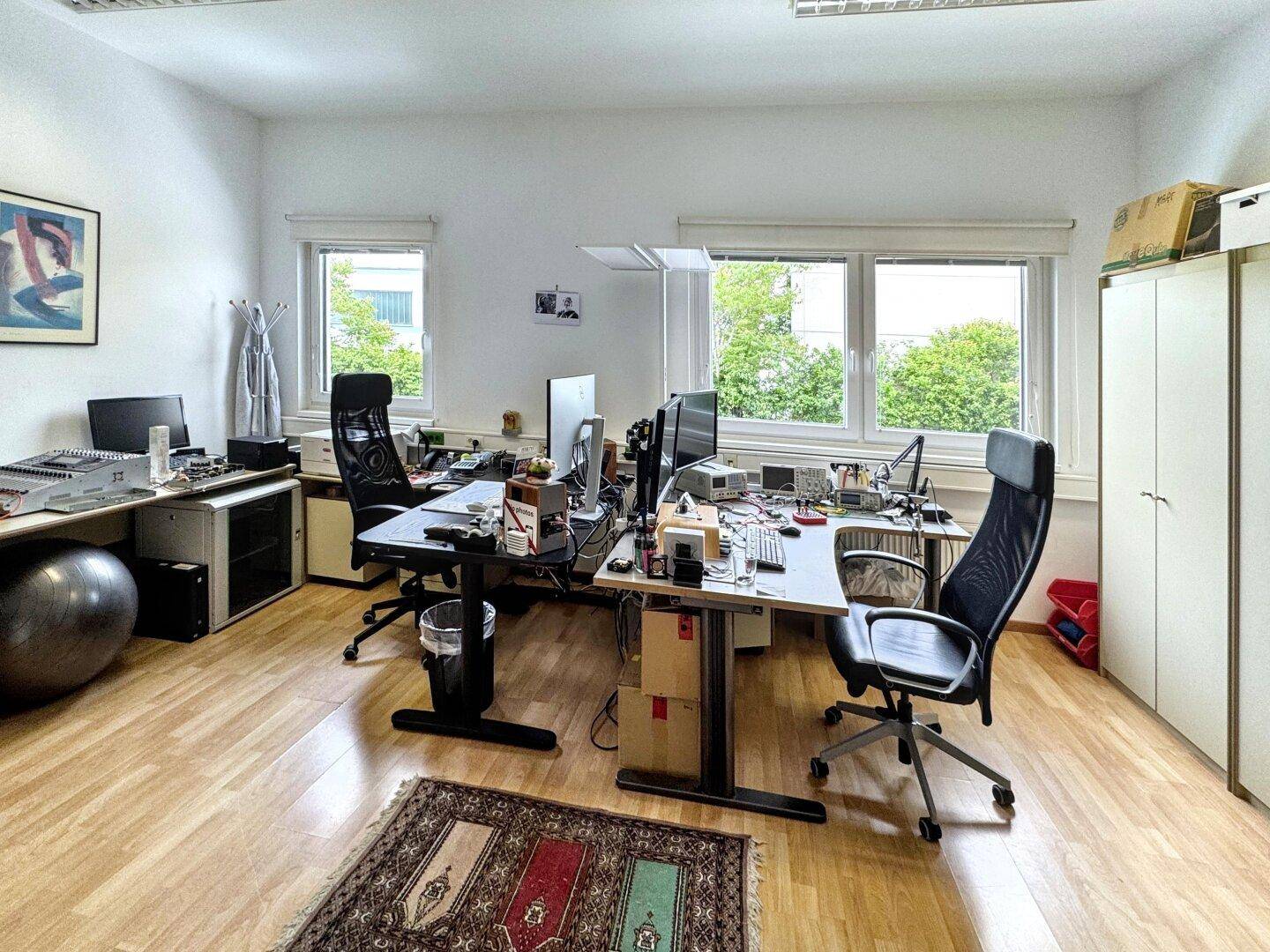 Geräumiges Büro mit mehreren Arbeitsplätzen, Holzfußboden und Blick ins Grüne durch die Fenster.