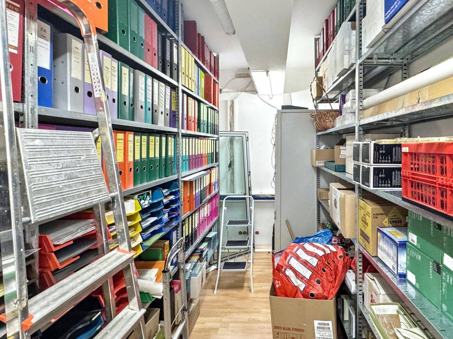 Lagerraum mit hohen Metallregalen, gefüllt mit Aktenordnern und Büromaterial.