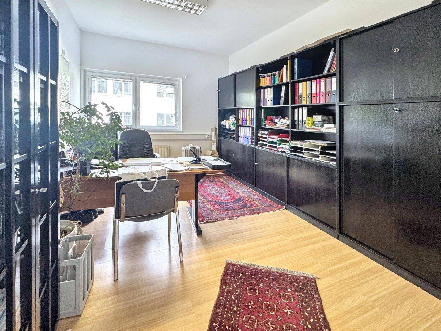 Büro mit dunklen Regalen voller Akten, einem Schreibtisch und Holzfußboden.