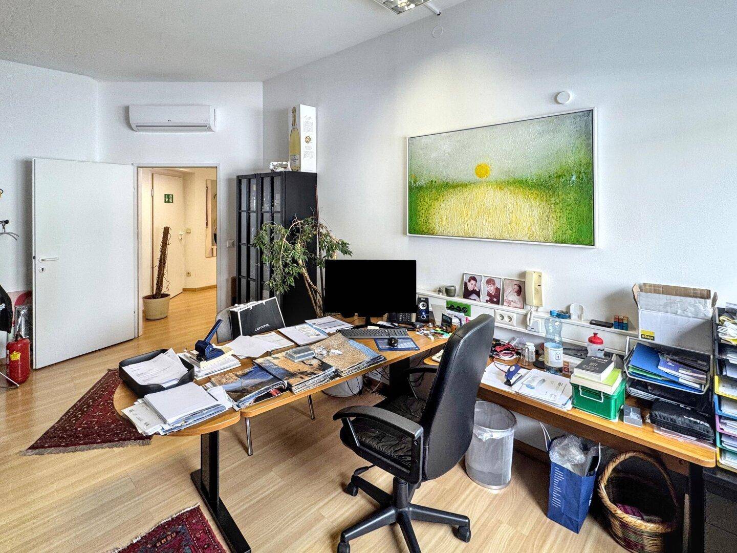 Büro mit einem großen Schreibtisch, Klimaanlage und einem Durchgang zu weiteren Räumen.
