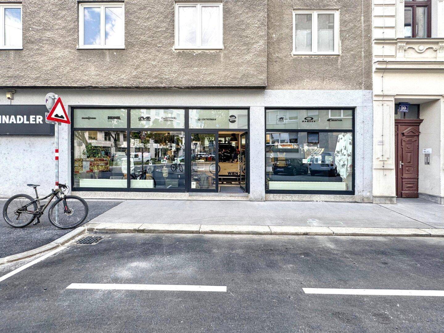 Vorderansicht des Geschäftslokals mit großen Schaufenstern und einem geparkten Fahrrad davor.