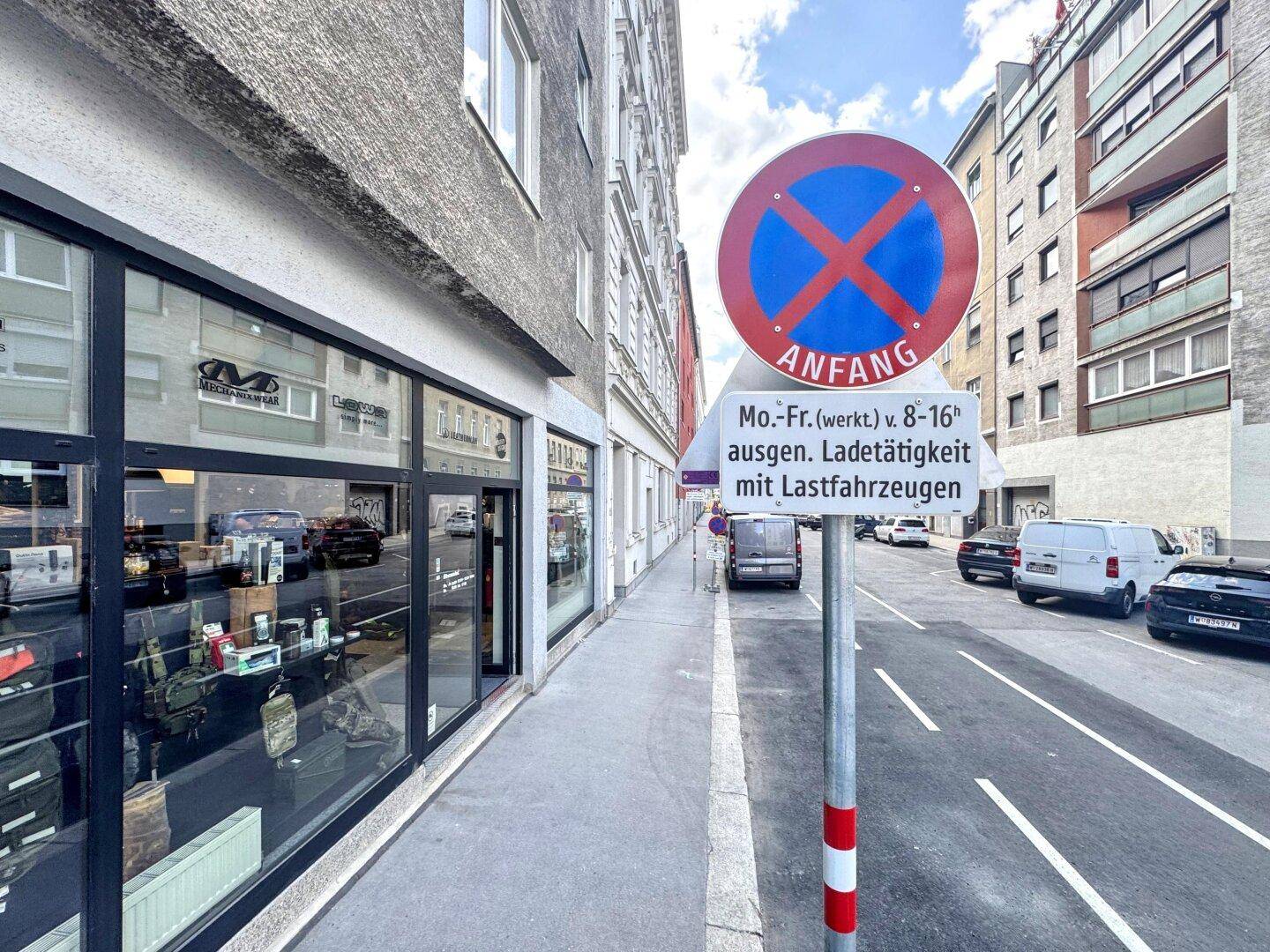 Blick die Straße hinunter mit einem Parkverbotsschild und geparkten Fahrzeugen vor den Gebäuden.