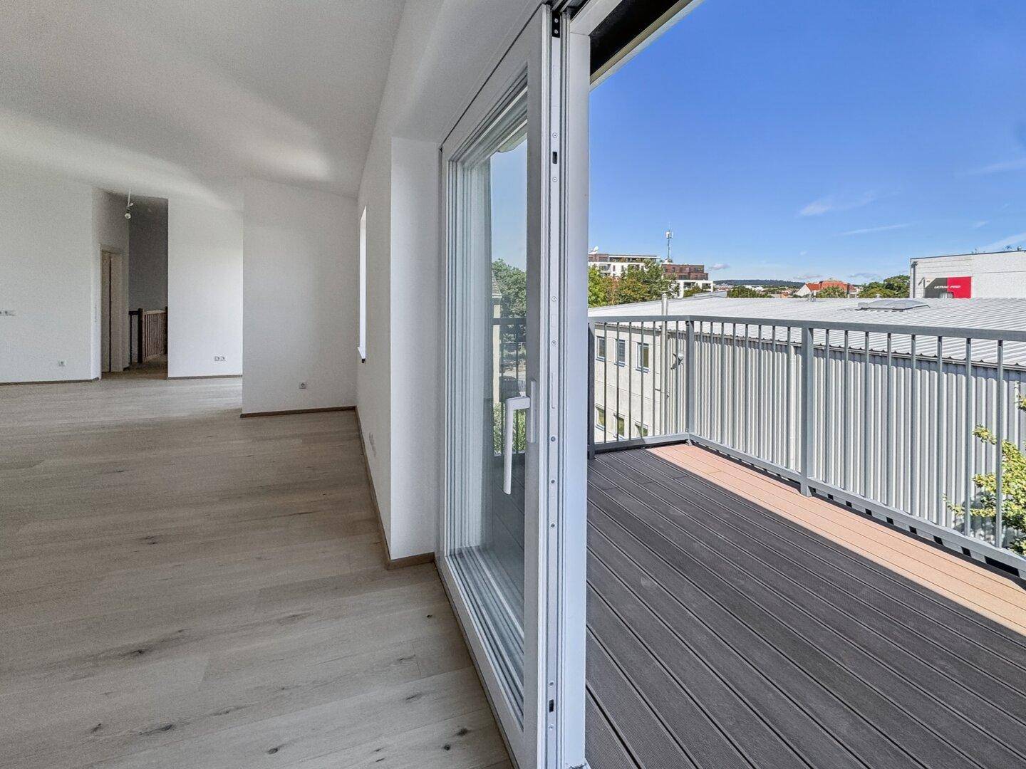 Blick vom Innenraum auf den Balkon mit dunklen Holzdielen und einem weiten Stadtblick.