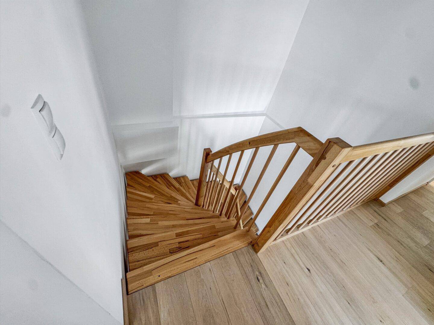 Elegante Holztreppe mit hellem Geländer, die die verschiedenen Etagen stilvoll miteinander verbindet.