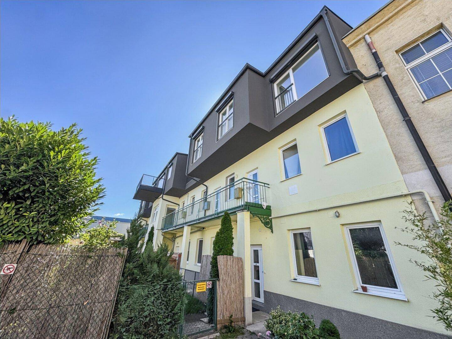 Moderne Gebäudefassade mit großen Fenstern und Balkonen unter klarem blauem Himmel.