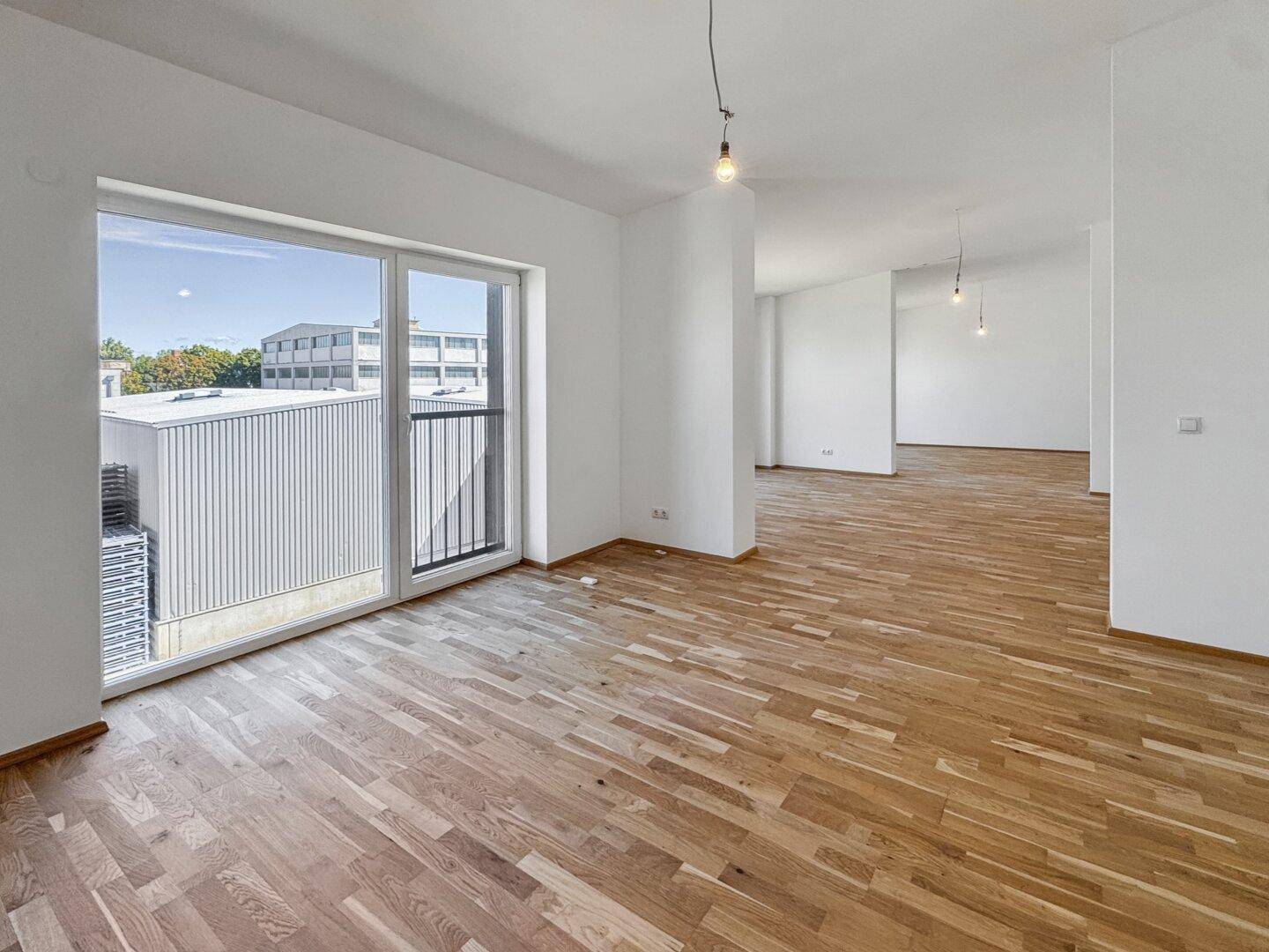 Geräumiger, heller Wohnbereich mit neuem Parkettboden und Zugang zu einem französischen Balkon.