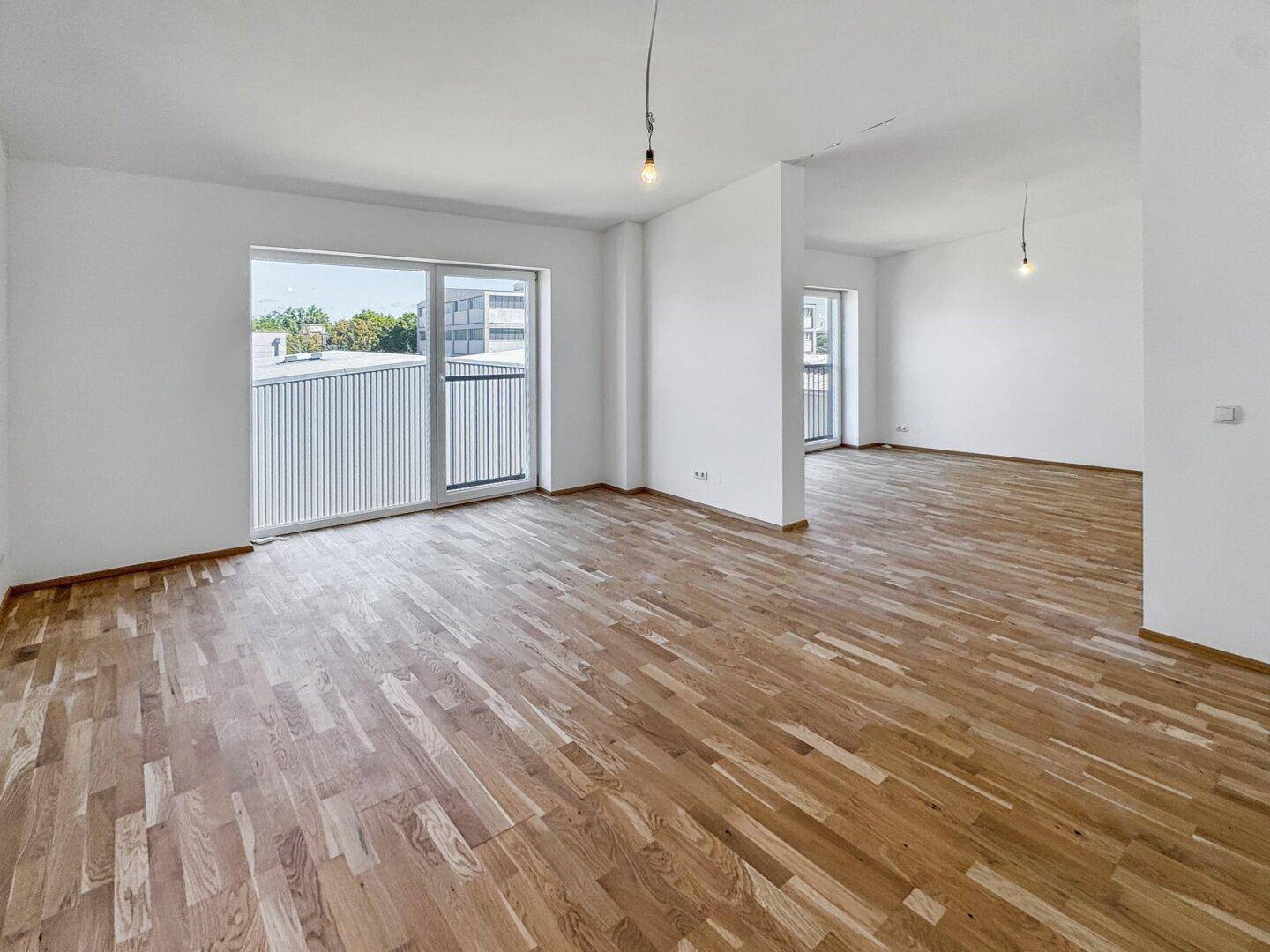 Großer, heller Wohnbereich mit Parkettboden und Zugang zu einem französischen Balkon.