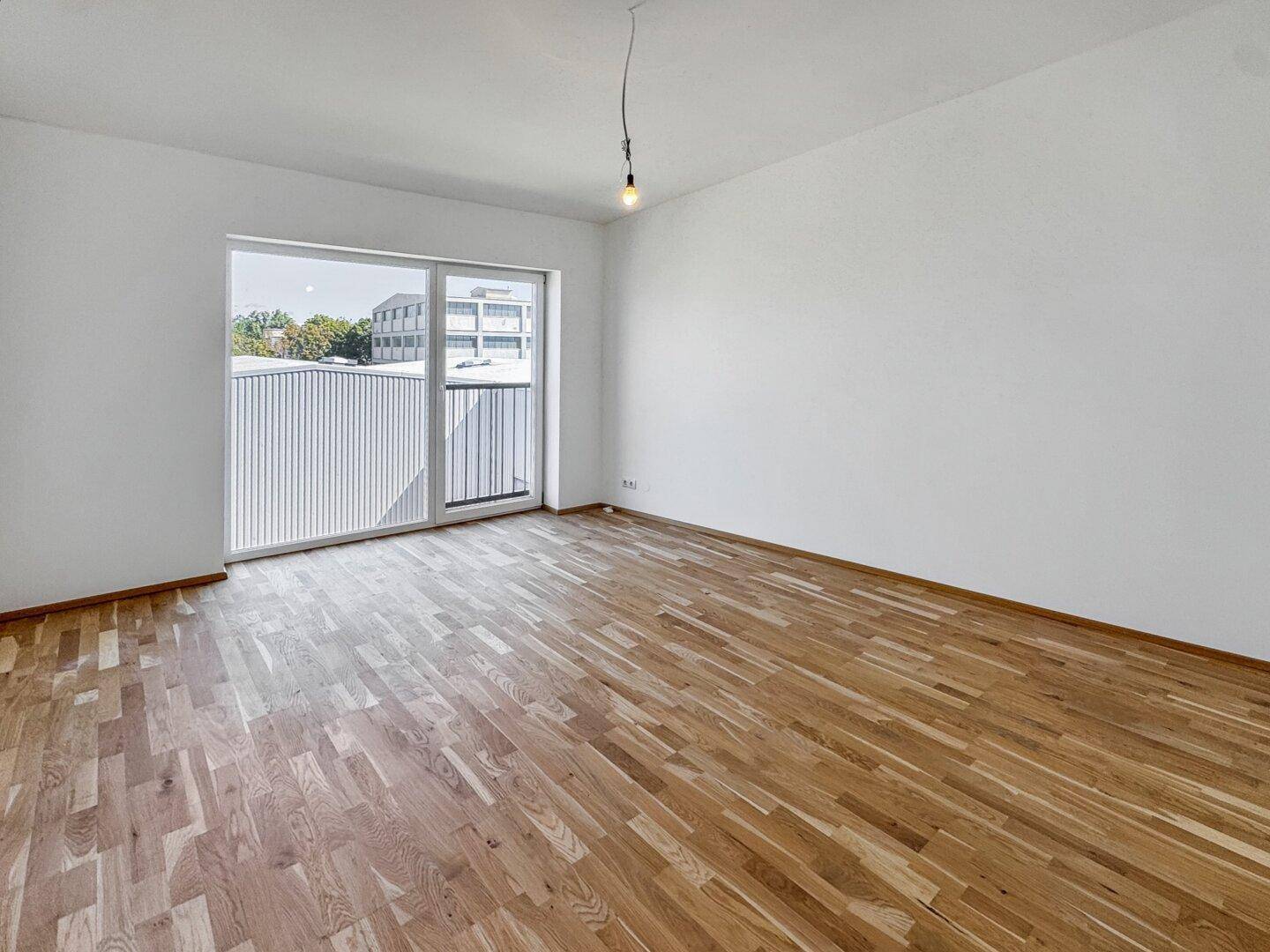 Geräumiges, helles Zimmer mit Parkettboden und großem Fenster, ideal für Wohnzwecke.