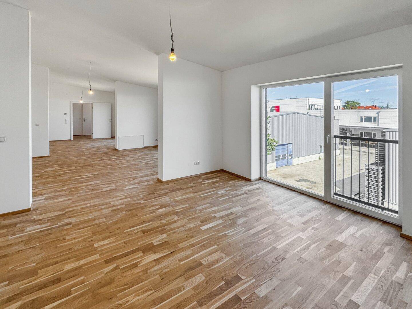 Heller Wohnbereich mit Parkettboden und großem Fenster, das viel Tageslicht hereinlässt.