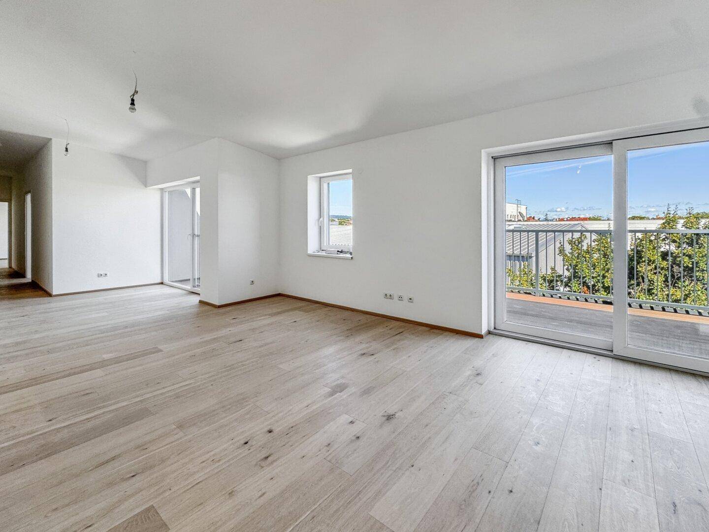 Heller Wohnbereich mit modernem Holzboden und Schiebetür zum Balkon, bietet weite Aussicht.