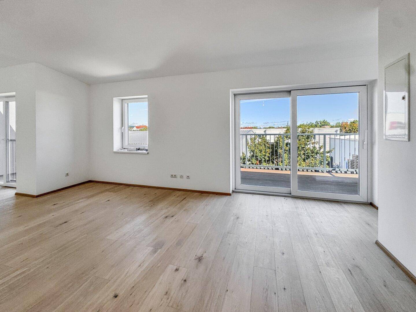 Geräumiger, heller Wohnbereich mit Holzboden und Schiebetür, die zu einem Balkon führt.