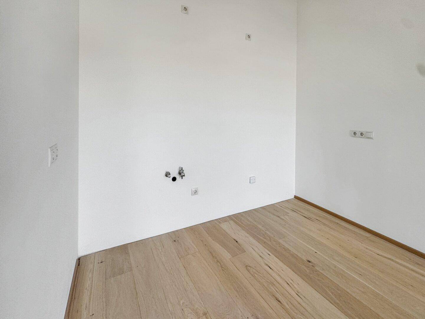 Leerer Raum mit Parkettboden und Anschlüssen für eine Küche, bereit für die Installation.