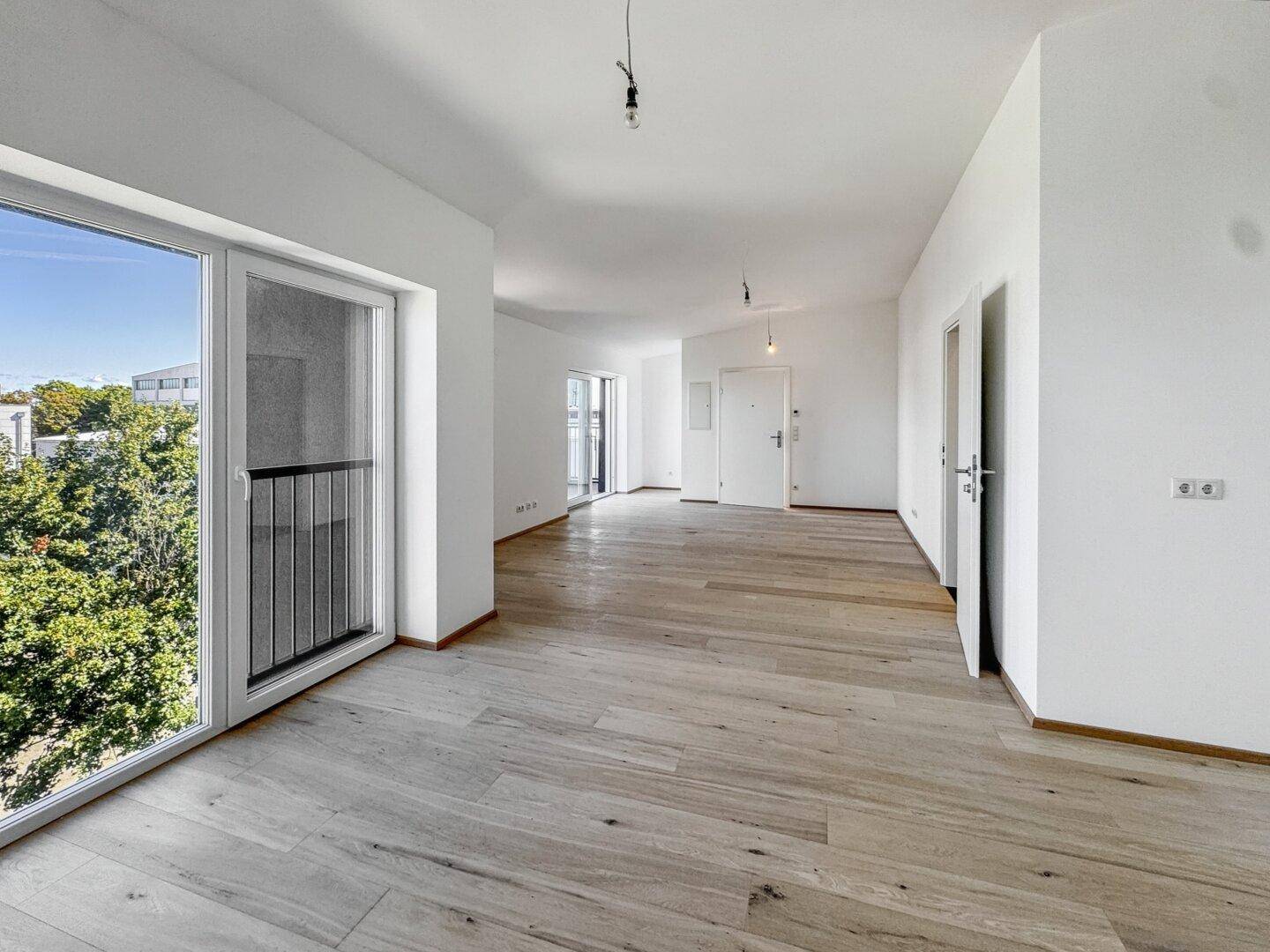 Geräumiger, heller Wohnbereich mit Parkettboden und Zugang zu einem Balkon, ideal für offenes Wohnen.