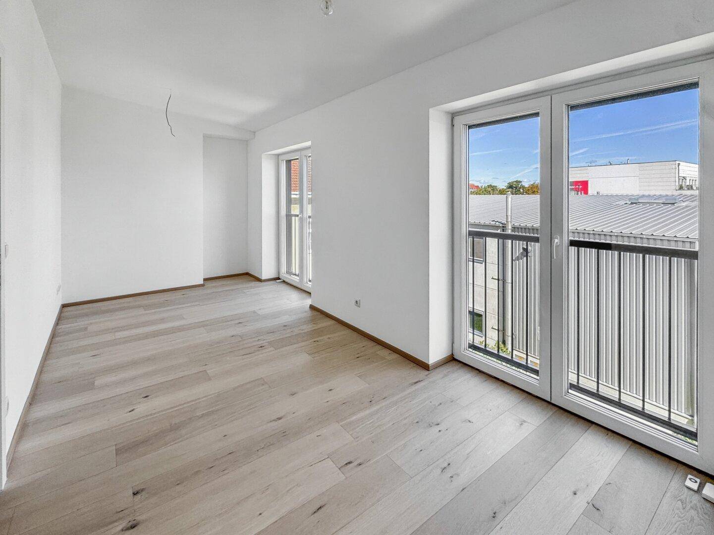 Geräumiger, heller Raum mit Holzboden und zwei französischen Balkonen, ideal für ein Wohnzimmer.