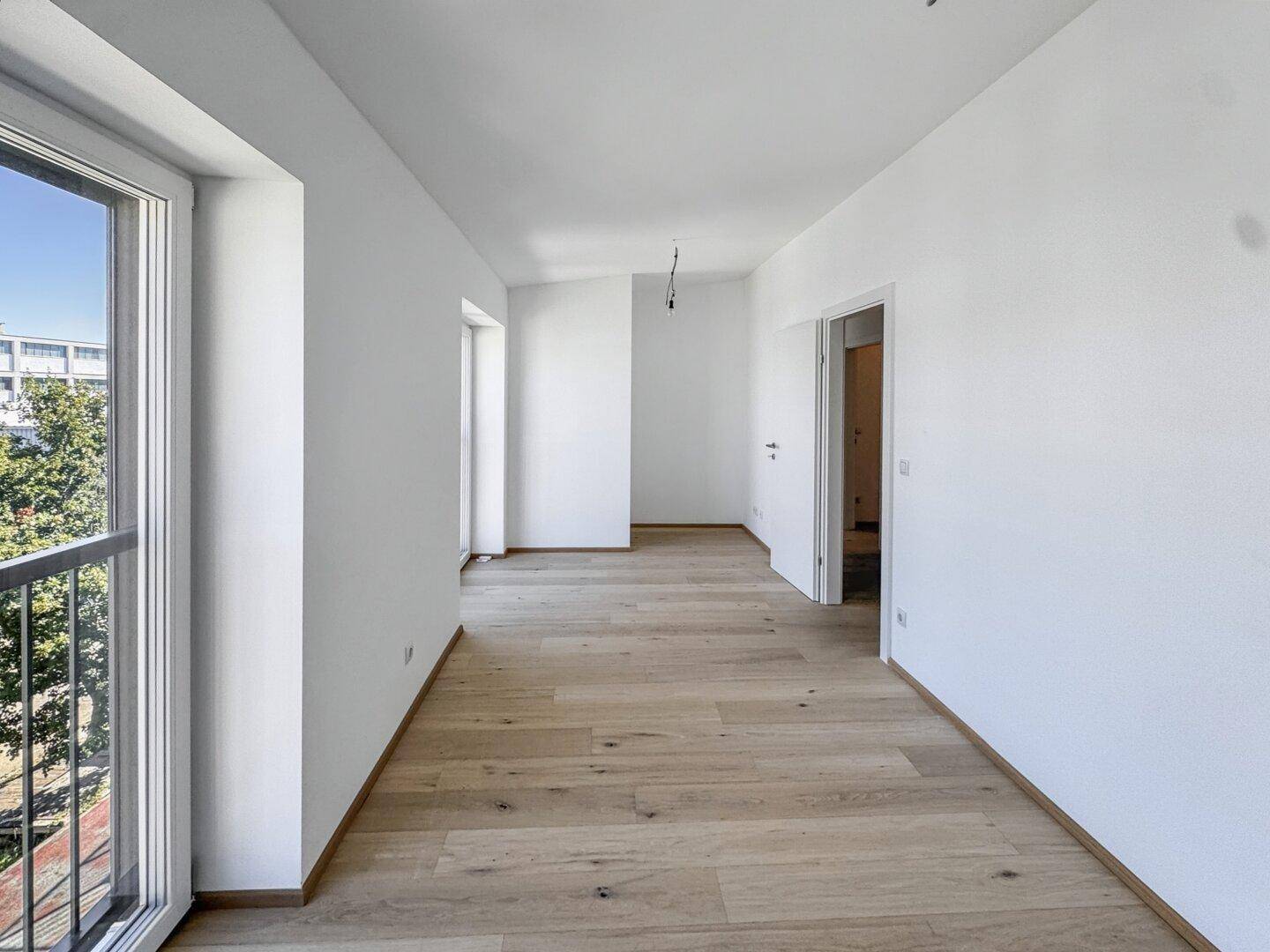 Lichtdurchfluteter Raum mit hellem Holzboden und Zugang zu einem französischen Balkon, bereit zur Einrichtung.