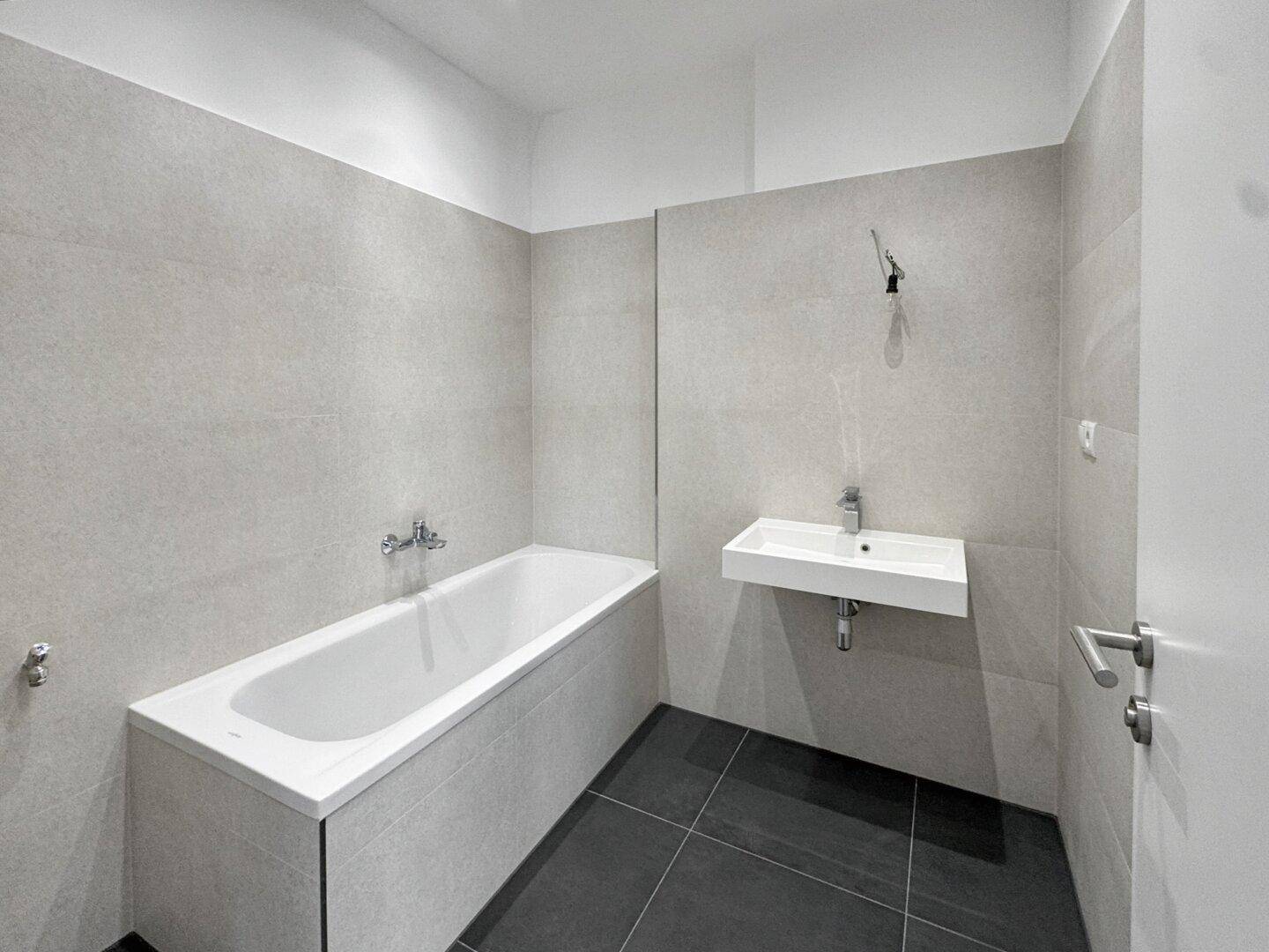 Modernes Badezimmer mit grauen Fliesen, einer Badewanne und einem schwebenden Einzelwaschbecken.