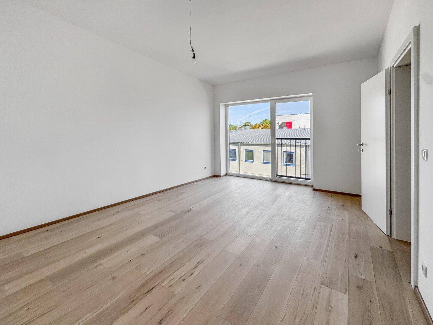 Heller, leerer Raum mit Holzboden und großem Fenster mit französischem Balkon, ideal für ein Schlafzimmer.