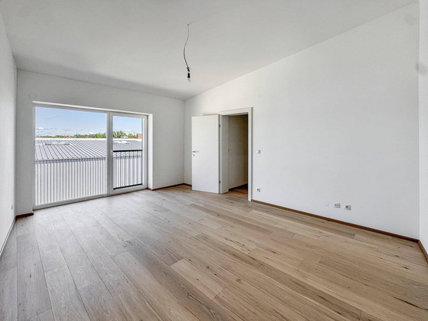 Geräumiger, heller Raum mit Holzboden und französischem Balkon, bietet viel natürliches Licht.
