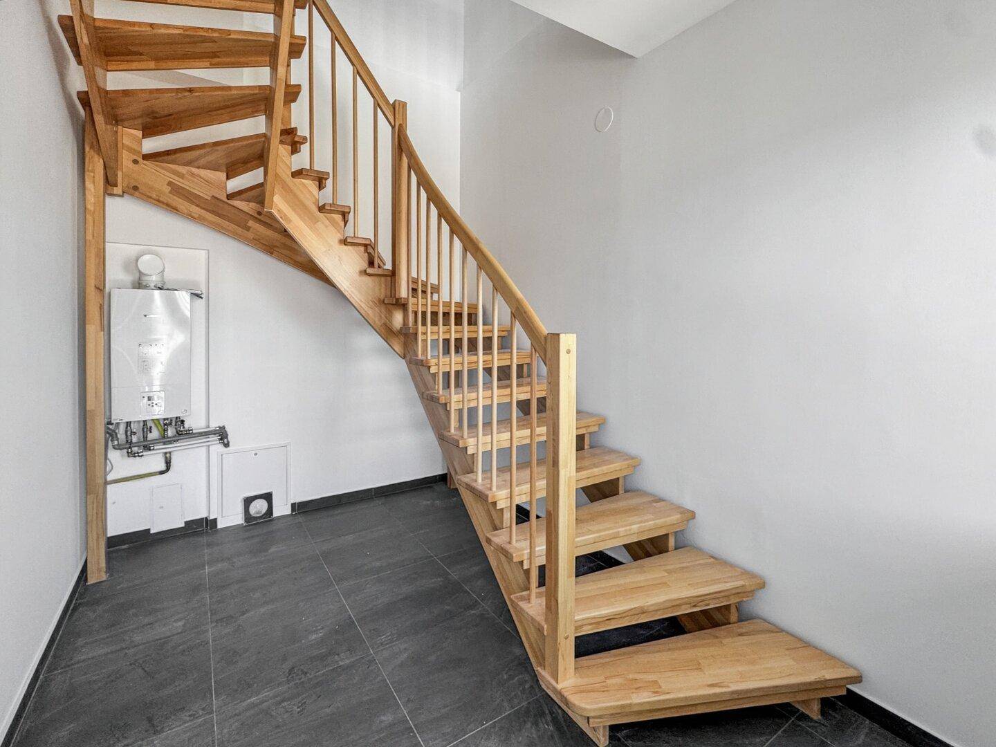 Holztreppe führt in einen Bereich mit Fliesenboden und sichtbarer Heizungsanlage.